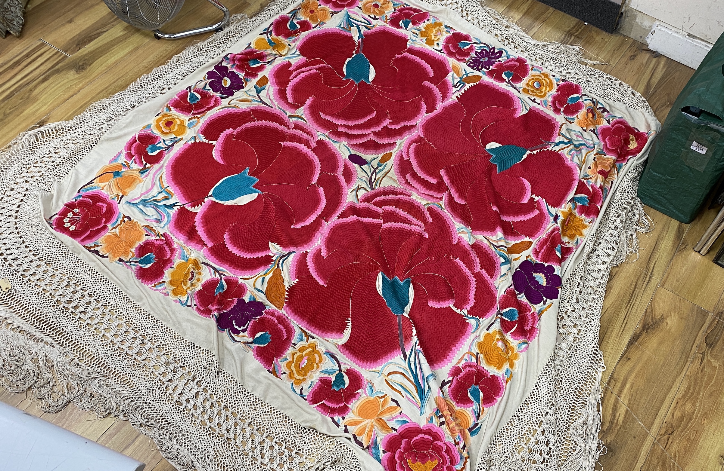 An unusual late 19th early 20th century Chinese cream silk shawl, embroidered with four huge bright pink and red flowers, surrounded with an embroidered floral border, all edged with a long cream silk tasselled fringe, 1